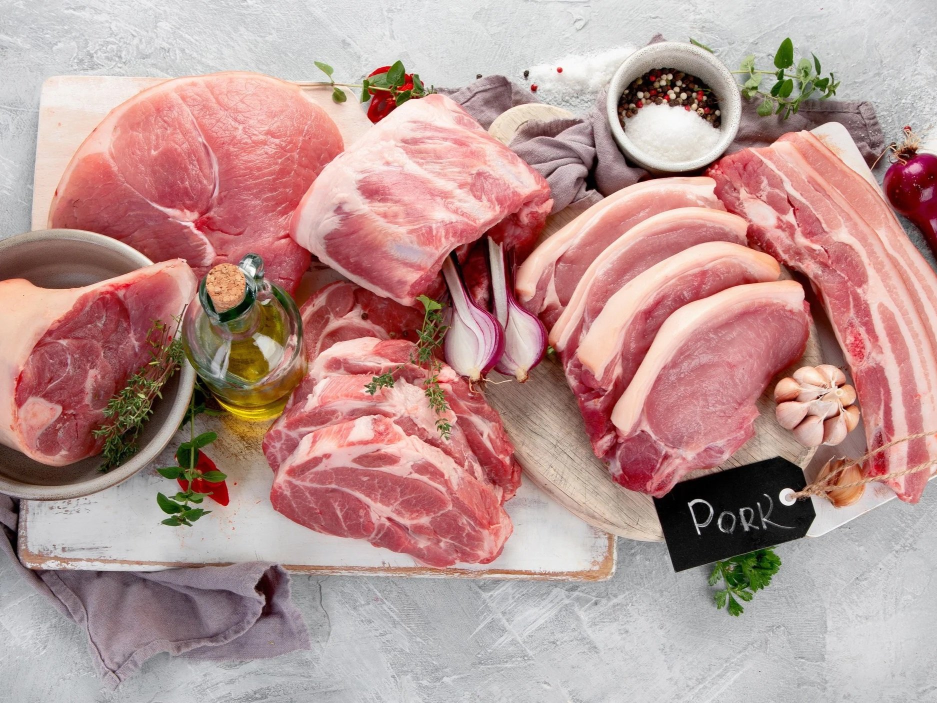 Falling+Sun+Ranch+-+Assortment+of+raw+pork+meat+on+light+grey+background.+Organic+gourmet+food+concept.+Top+view,+flat+lay Assorted cuts of fresh pork meat displayed on a wooden board, featuring pork chops, belly, and shoulder, accompanied by herbs, garlic, and olive oil for culinary preparation.